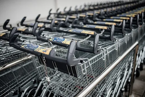 A row of empty shopping carts is neatly arranged in a grocery store. The carts feature a locking mechanism and display a numerical keypad, r